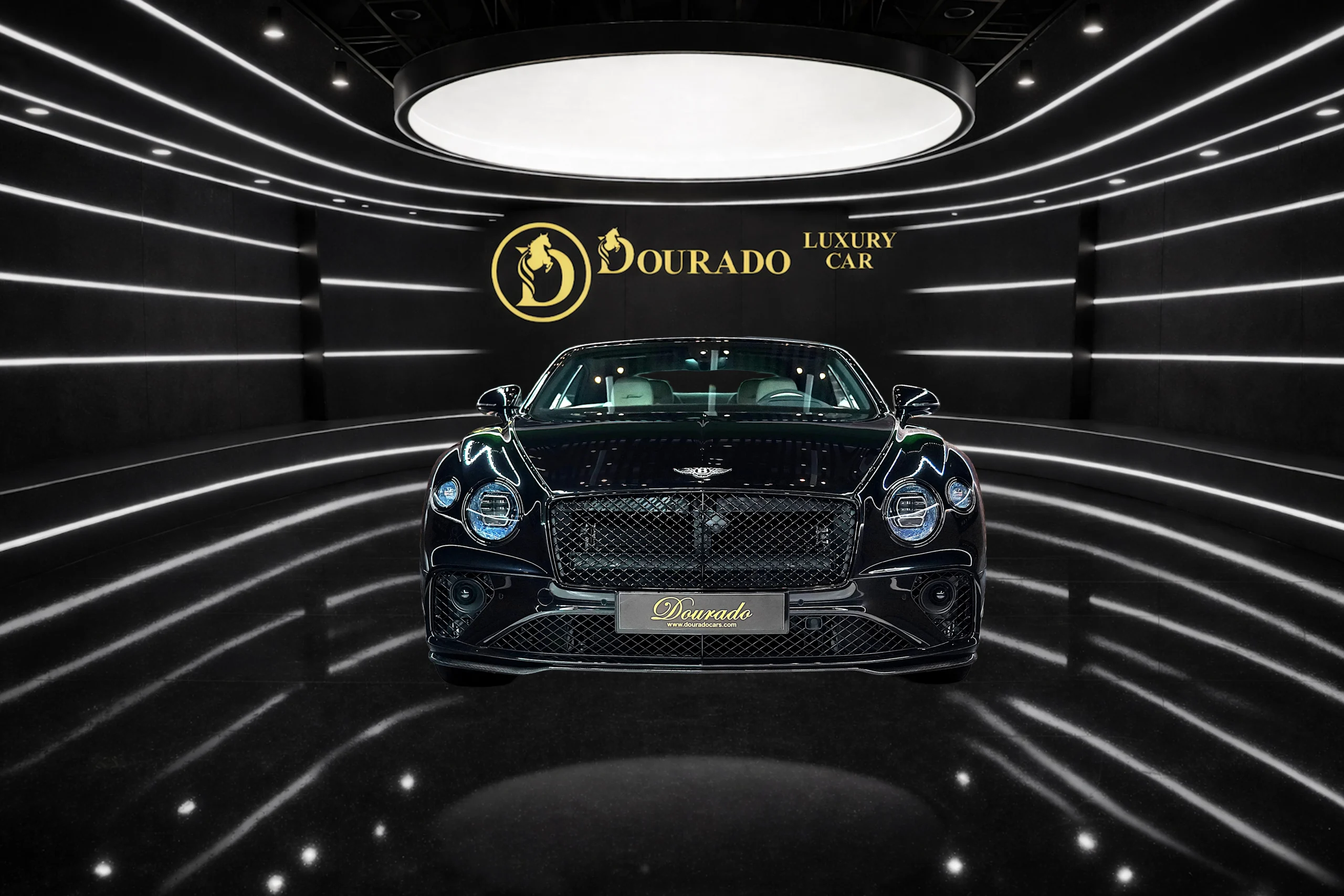 Front view of a sleek black luxury car in a neon-lined black showroom with a gold Dourado logo on the wall.