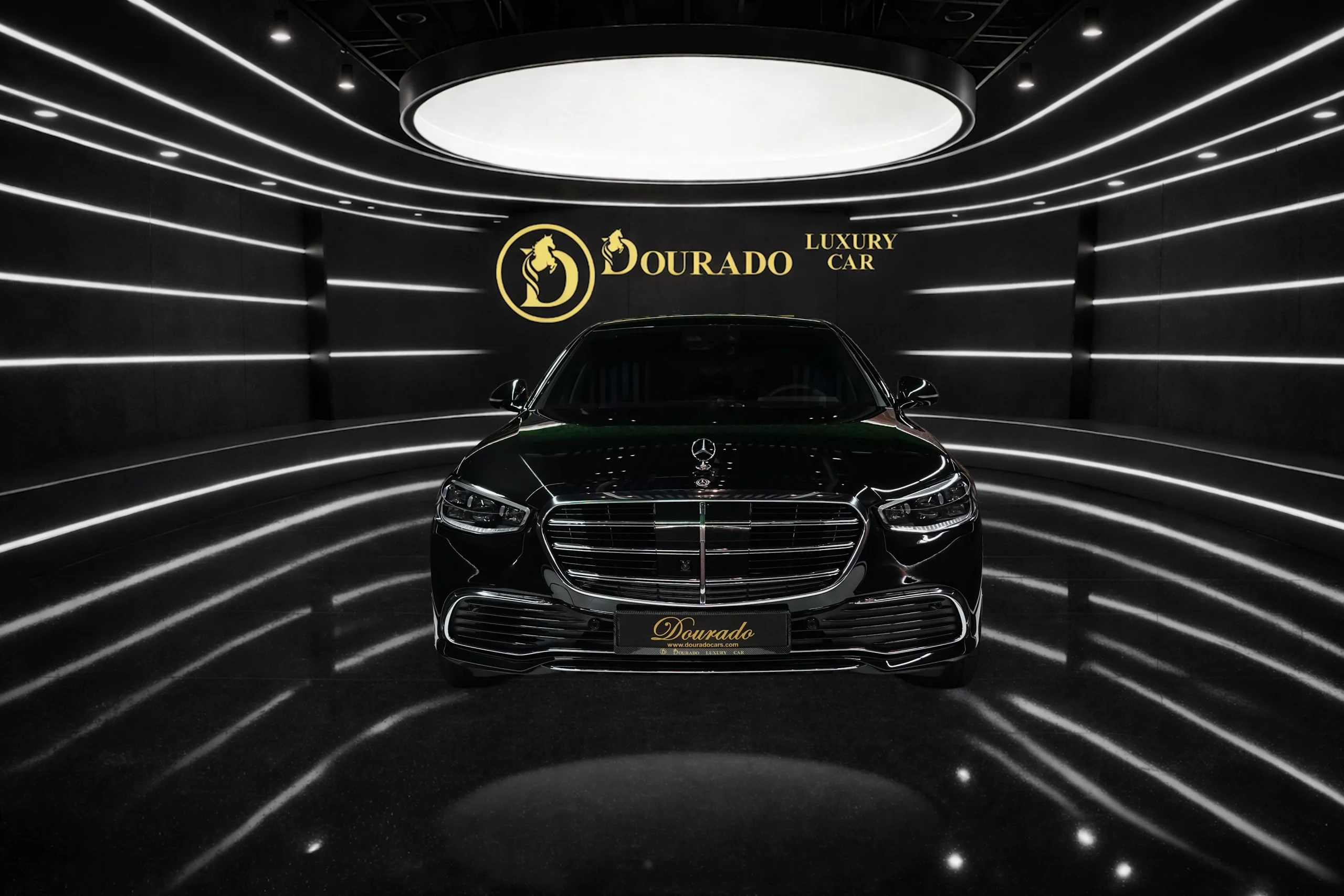 Black Mercedes-Benz luxury sedan in a futuristic showroom with curved white light strips and a gold Dordado logo on the back wall.