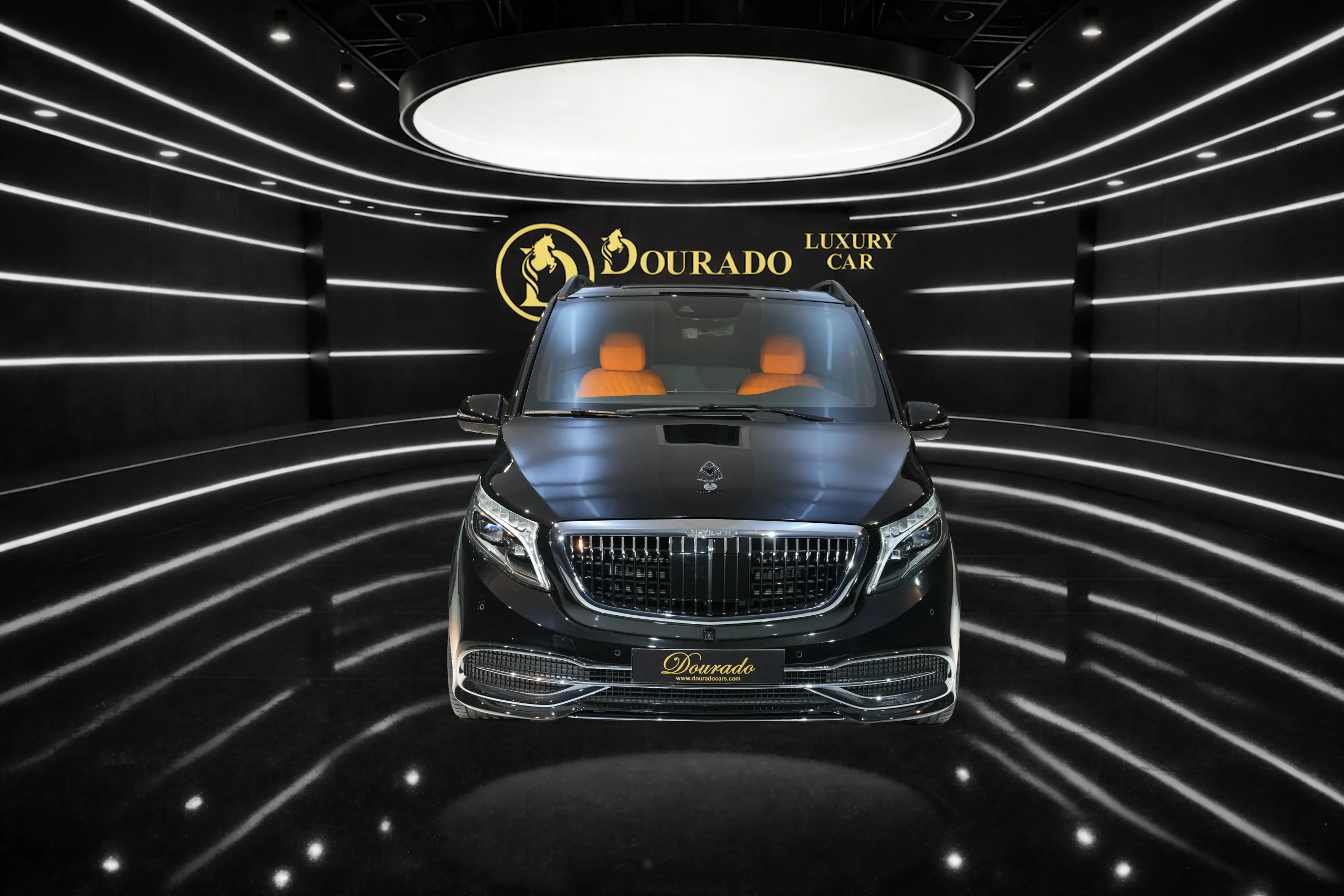 Front view of a black luxury SUV with tan interior on a glossy showroom floor, curved white light stripes and a gold Dourado logo in the background.